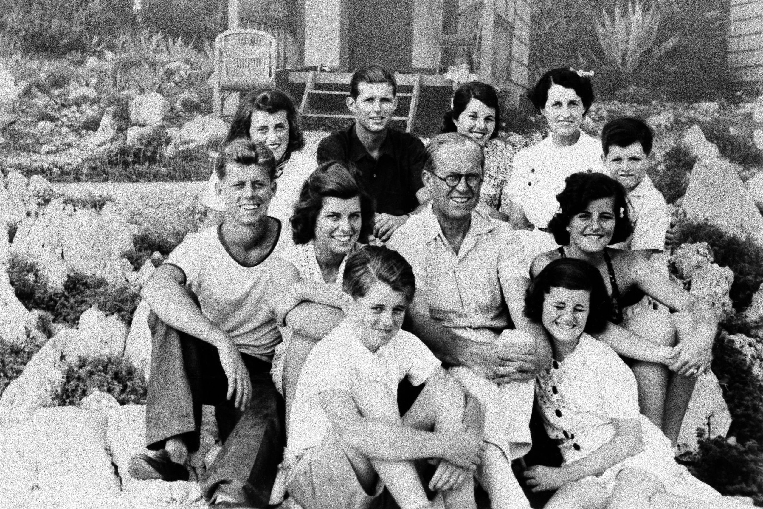 Joseph P. Kennedy senior (d. 1969), USA's ambassadør til Storbritannien 1938-1940, sidder i midten omringet af den nærmeste familie. Med uret fra venstre side i bunden: Robert, Eunice, John (USA's 35. præsident), Kathleen, Joe Jr., Rosemary, Teddy, Patricia og Jean. 